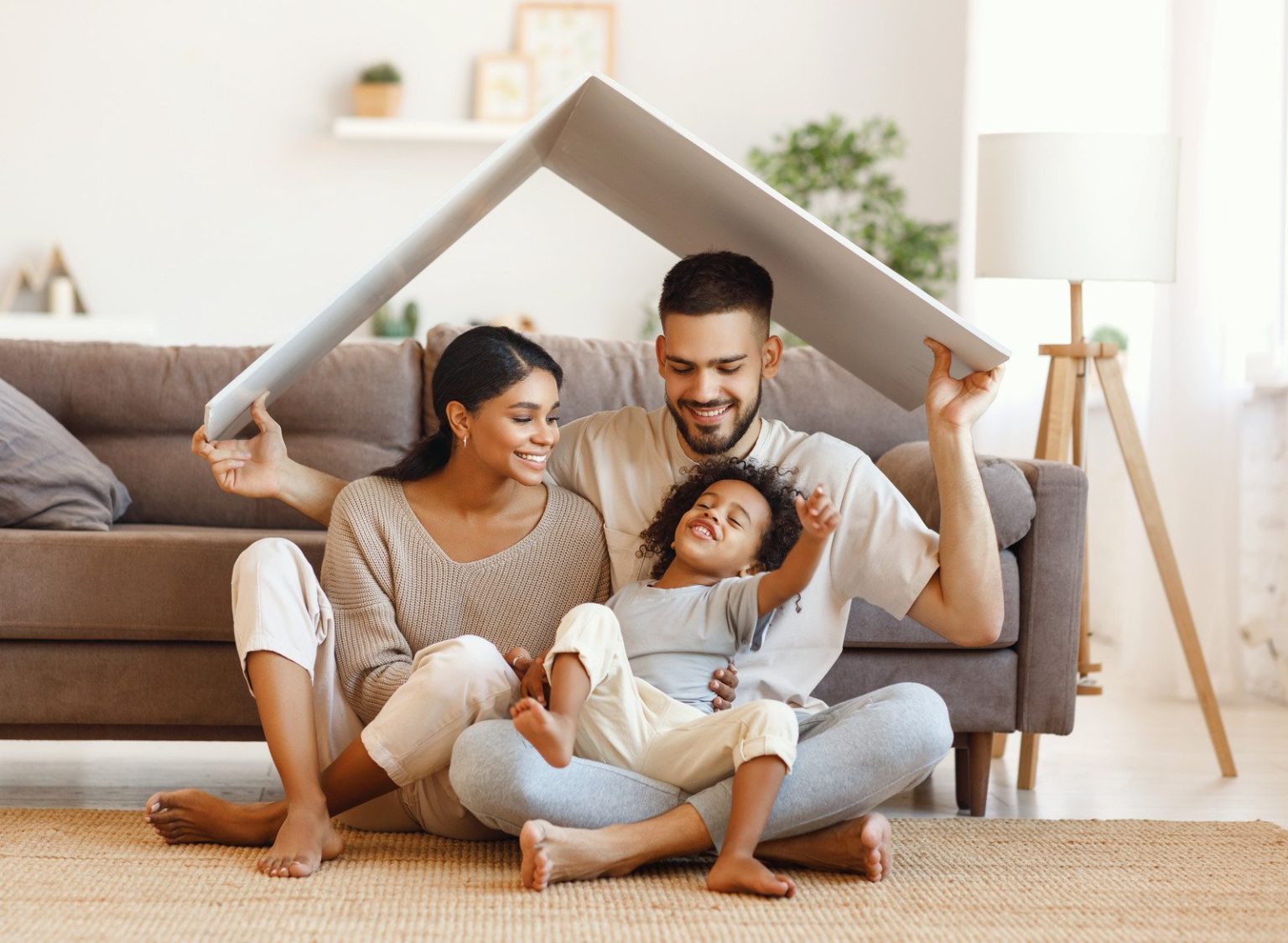 two parents and their young sun sitting underneath a mock cardboard roof smiling in the living room