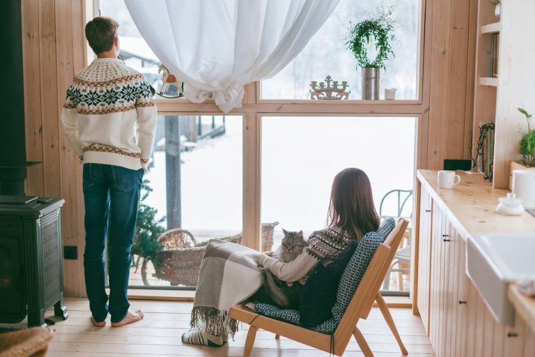 a young woman sitting in a window bench holding a cup of tea while looking outside at the snow in the daytime