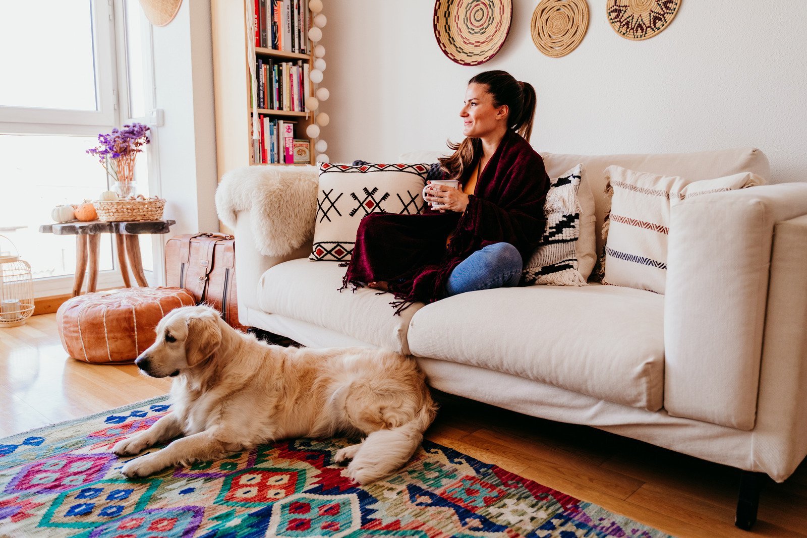 a woman in a black sweater sitting on a couch with a mug of tea while a dog lays at her feet