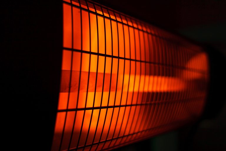 Close-up of an electric heater with orange glowing elements behind a grid, creating a warm, inviting ambiance in a dark setting.