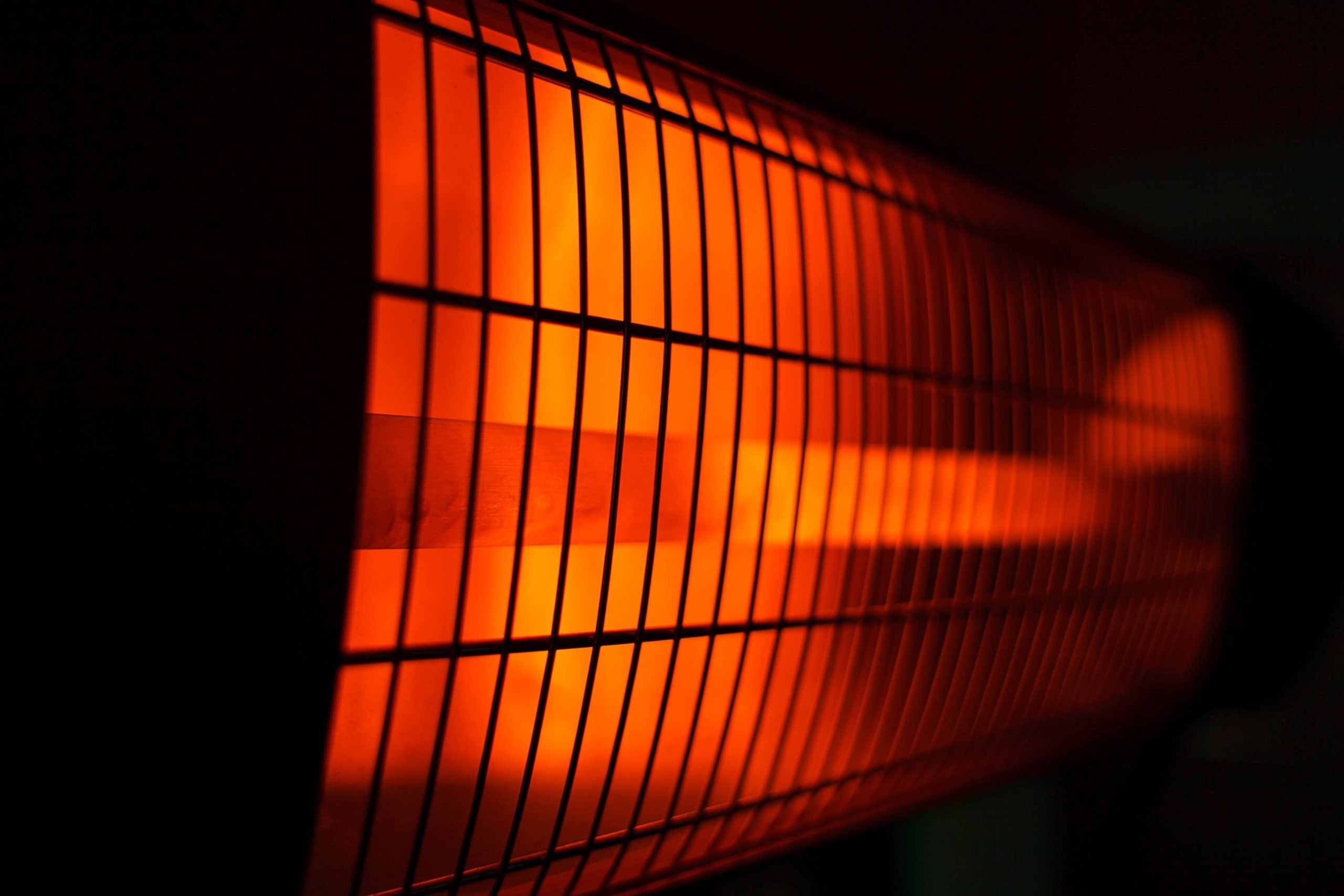 Close-up of an electric heater with orange glowing elements behind a grid, creating a warm, inviting ambiance in a dark setting.
