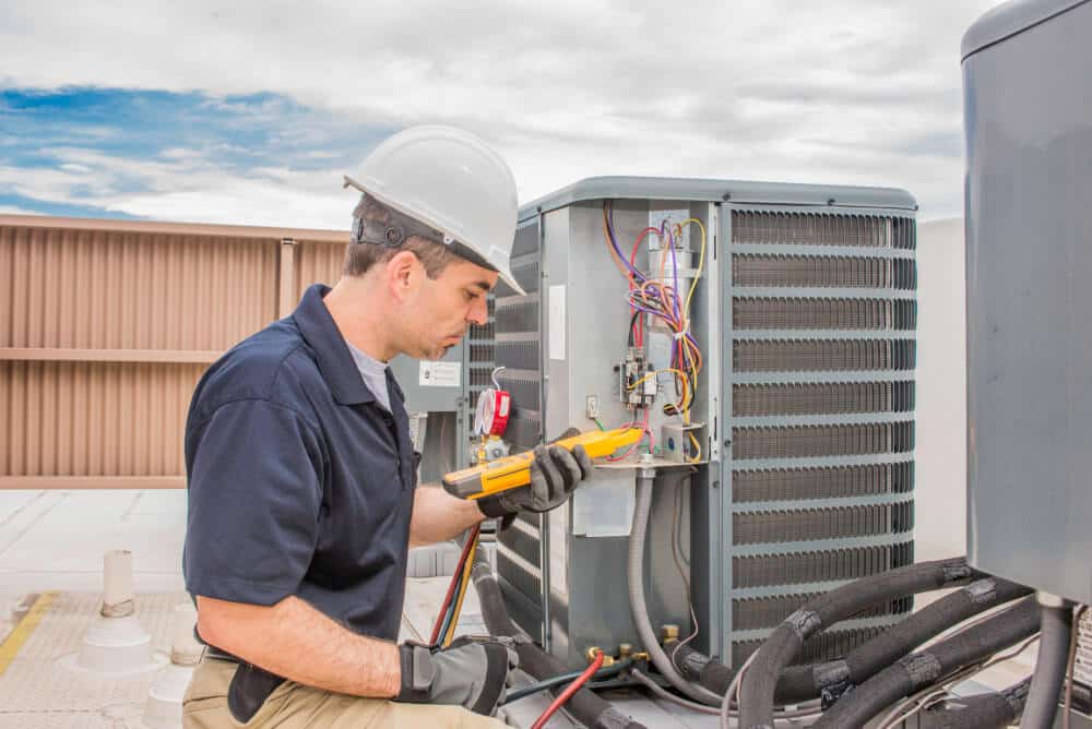 An HVAC technician in a white hard hat inspects the electrical wiring of an outdoor air conditioning unit to identify potential AC short cycle causes.
