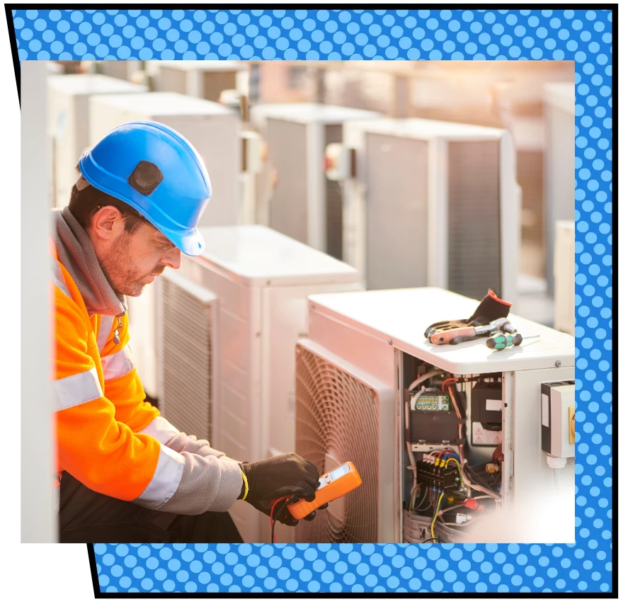 A worker in a blue hard hat and orange safety jacket repairs an outdoor air conditioning unit, using tools while inspecting electrical components.