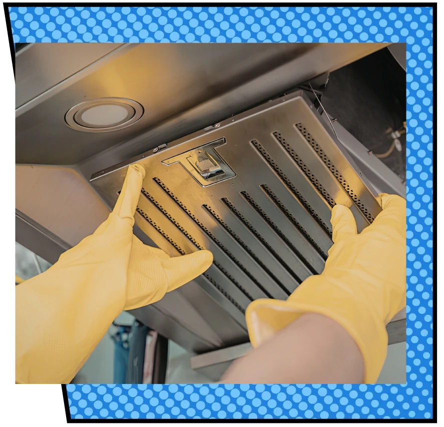A person wearing yellow rubber gloves is cleaning a stainless steel kitchen exhaust hood. The scene conveys cleanliness and attention to detail.