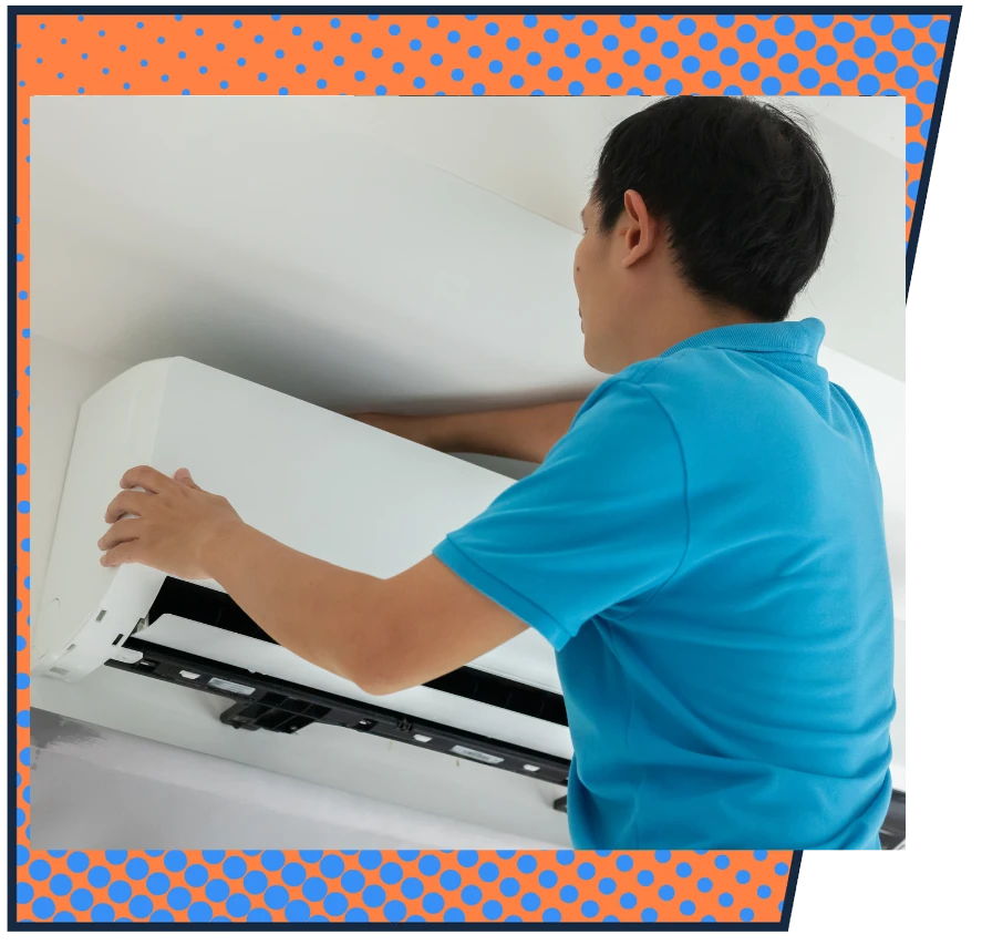 A person in a blue shirt installs or repairs a white wall-mounted air conditioner, focused and working carefully. The background has a blue and orange dotted border.